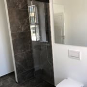 Nyt badeværelse med mørke fliser og glasvæg efter renovering