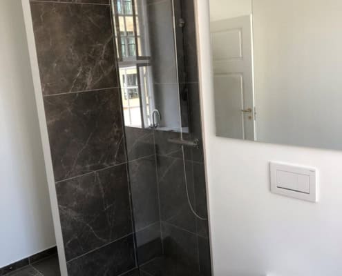 Nyt badeværelse med mørke fliser og glasvæg efter renovering