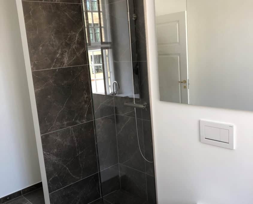 Nyt badeværelse med mørke fliser og glasvæg efter renovering